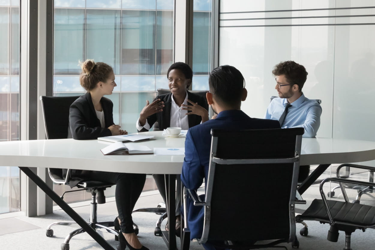 Three business professionals seated at a conference table in a modern office setting, engaged in discussion.